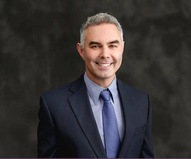 a man wearing a suit and tie smiling at the camera